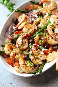 a white bowl filled with shrimp, asparagus and olives