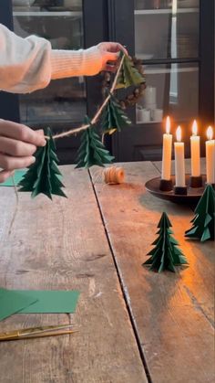 someone decorating christmas trees on a table with candles in front of the candle holders