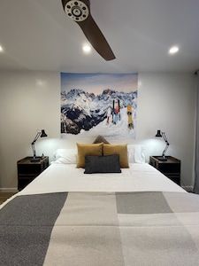 a bedroom with a ceiling fan and large painting on the wall above the headboard