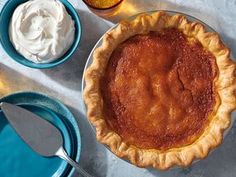 an apple pie with whipped cream on the side and two blue bowls filled with ice cream