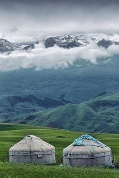 two yurts sitting in the middle of a green field with mountains in the background