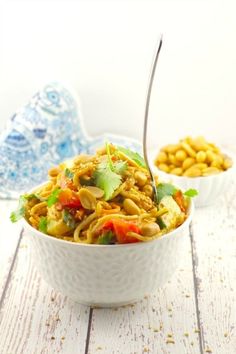 a bowl filled with noodles and vegetables on top of a white wooden table next to another bowl