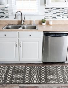 a kitchen with a sink, dishwasher and rug on the floor in front of it