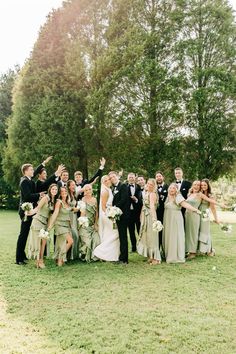 a large group of people in formal wear posing for a photo on the grass with trees in the background