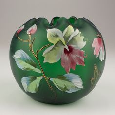 a green vase with pink and white flowers painted on the front, sitting on a table