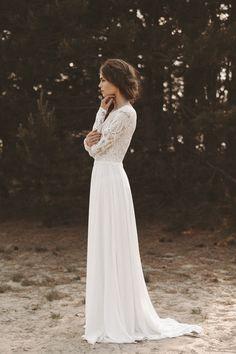 a woman wearing a white dress standing in front of trees