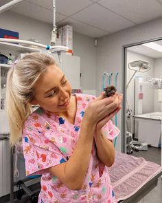 a woman in pink scrubs holding a small bird on top of her arm and looking at the camera