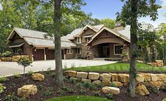 a large house surrounded by lots of trees and rocks in front of it's driveway