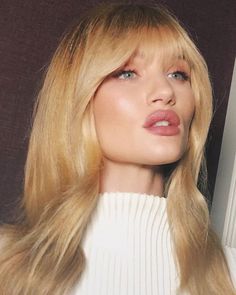 a woman with long blonde hair wearing a white sweater and pink lipstick on her lips