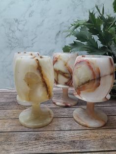 three marbled vases sitting on top of a wooden table next to a potted plant