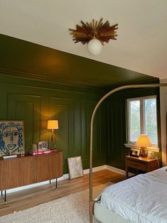 a bedroom with green walls and wooden flooring has a lamp on the side table