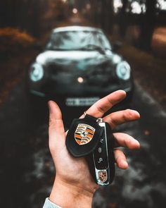 a hand holding a car key in front of a parked car on a road with trees and grass