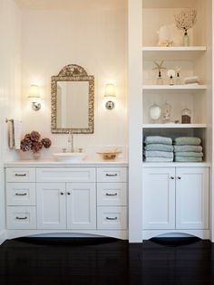 a bathroom with white cabinets and black flooring is pictured in this image, there are towels on the shelves