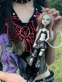 a woman holding a doll in her hands and wearing goth clothes with black accessories on it