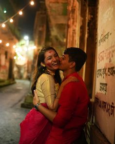 a man and woman embracing each other in front of a wall with lights on it