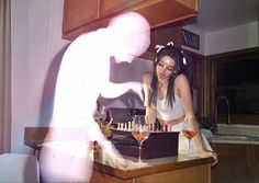 a woman standing in front of a counter with wine glasses on it and a shadow of a person behind her