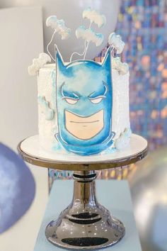 there is a cake with a batman face on it and balloons in the back ground