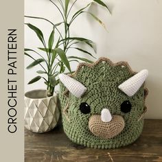 a green crocheted bag with horns on it sitting next to a potted plant