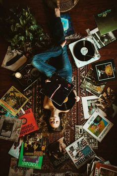 a man laying on top of a rug covered in books and magazines next to a record player