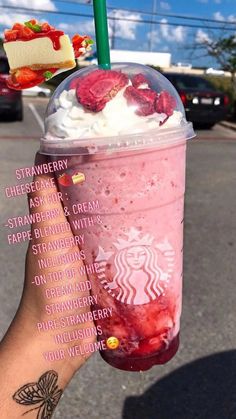 a person holding up a pink drink with whipped cream and strawberries in it on the street