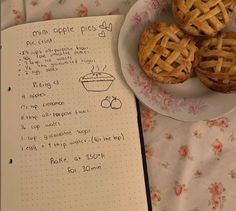 three small pies on a plate next to an open recipe book with writing in it