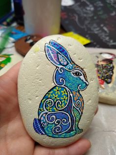 a hand holding a painted rock with a rabbit on it