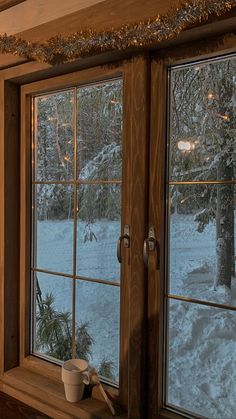 there is a cup sitting on the window sill in front of the snow covered trees