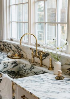 a kitchen sink with marble counter tops and gold faucets in front of a window