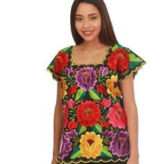 a woman is wearing a colorful top with flowers on the front and side, she has her hands in her pockets