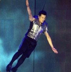 a man in silver shirt and black pants on stage with arms outstretched up to the side