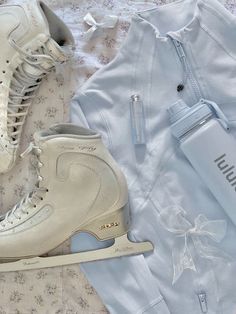 a pair of white ice skates sitting on top of a bed next to a water bottle