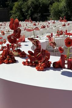 a table topped with lots of white tables covered in red flowers and vases next to each other