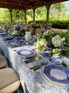 a long table with blue and white plates, silverware and flowers in vases