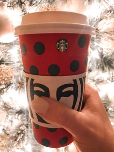 a hand holding a starbucks cup with a ladybug design on it, in front of a christmas tree