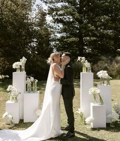 a bride and groom kissing in front of white flower arrangements on the lawn at their wedding