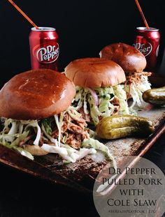 three pulled pork sandwiches with coleslaw and pickles on a tray next to two sodas