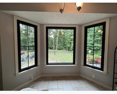 an empty room with three large windows and tile flooring in front of the window