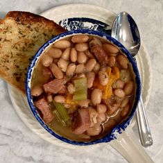 a bowl of beans and ham soup next to a piece of bread