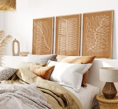 a bed with pillows and blankets on top of it next to two framed art pieces