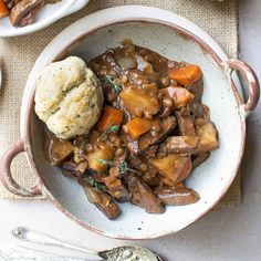 a bowl filled with meat and vegetables on top of a table next to two silver spoons