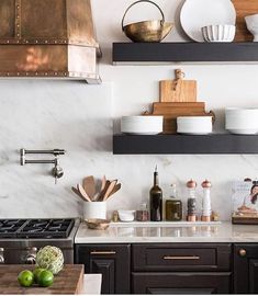 a kitchen with black cabinets and white marble counter tops, gold accents on the shelves