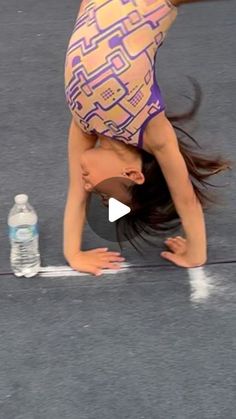 a woman doing a handstand on top of a tennis court with a bottle of water