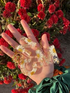 a person's hand with flowers and rings on it, surrounded by red flowers