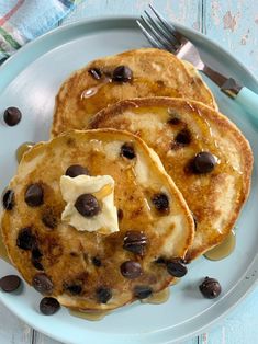 three pancakes with chocolate chips and butter on a blue plate next to a knife and fork