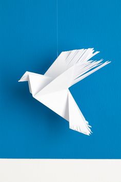 an origami bird hanging from a string on a blue wall with white paint