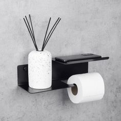 a toilet paper holder with some sticks sticking out of it and a cell phone on the wall