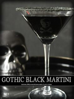 a black drink in a martini glass on a table with a skull head behind it