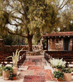 an outdoor ceremony setup with chairs and rugs on the ground in front of a tree