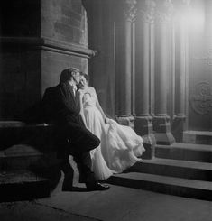 black and white photograph of a bride and groom sitting on steps in front of a building