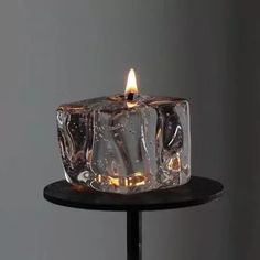 a lit candle sitting on top of a black table with ice cubes around it